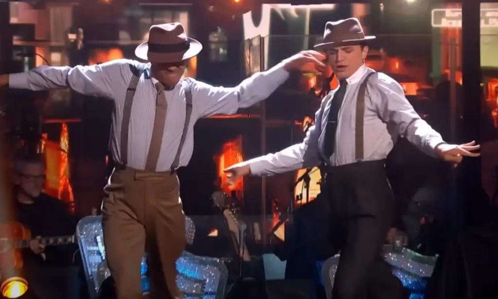 Layton Williams y Nikita Kuzmin visten trajes compuestos por una camisa, tirantes, pantalones y sombrero mientras bailan juntos durante una actuación en Strictly Come Dancing de la BBC.