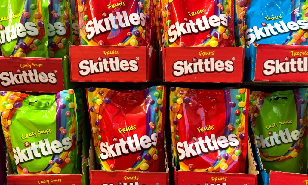 Un juego de paquetes de Skittles en un supermercado, se exhiben paquetes rojos y verdes.