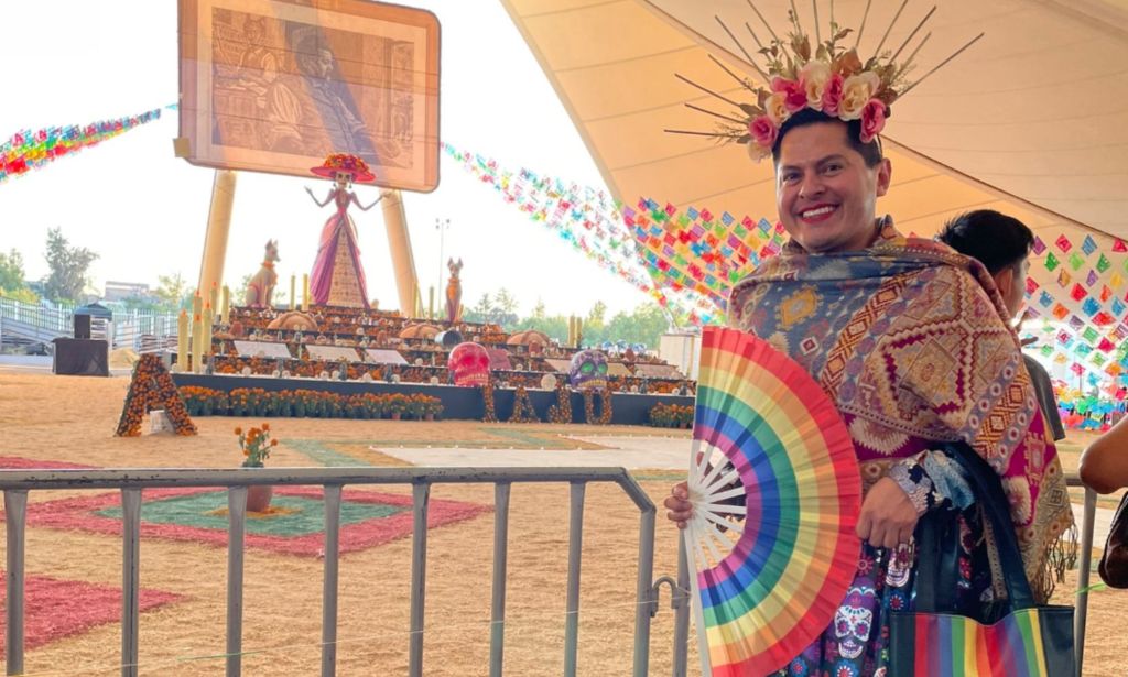 Jesús Ociel Baena viste una falda y un top coloridos mientras posan con un abanico LGBTQ+ de arcoíris.  Se encuentran entre las celebridades, agentes de cambio y aliados LGBTQ+ que murieron en 2023.