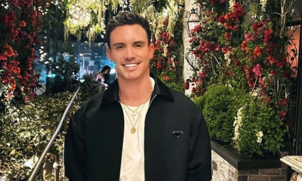 El modelo e influencer gay Jeff Thomas, que se encuentra entre las celebridades LGBTQ+ que murieron en 2023, viste una camisa blanca y una chaqueta negra mientras sonríe y posa para una foto al aire libre.