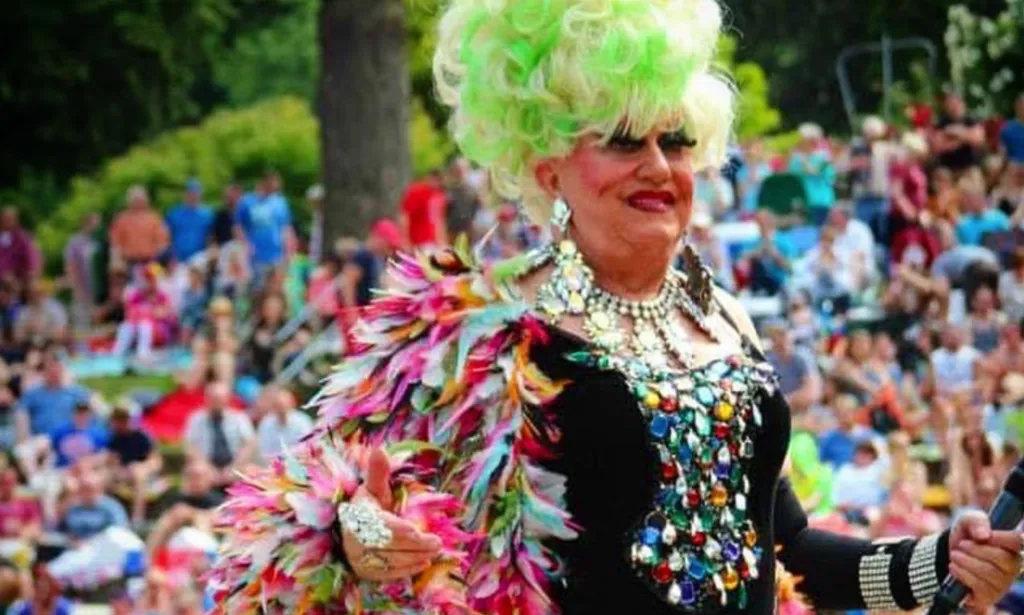 Una foto de Darcelle XV, una celebridad LGBTQ+ que murió en 2023, con una peluca verde y saludando a una multitud.