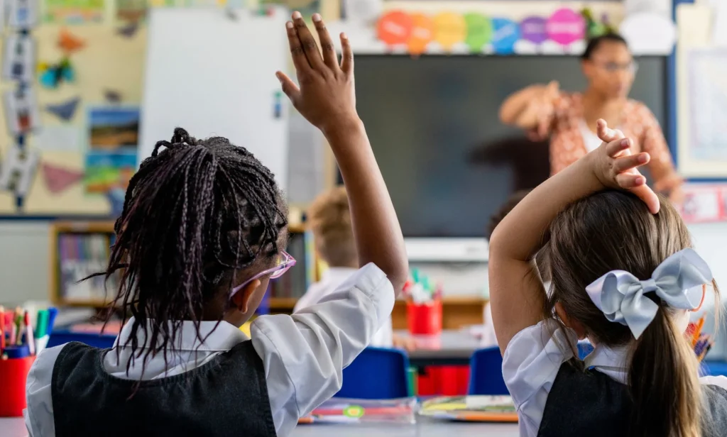 Two children raise their hands in a school classroom.