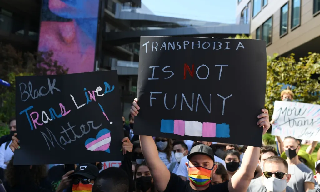 Un grupo de personas sostiene carteles en apoyo a la comunidad trans después de que Ted Sarandos de Netflix defendiera a Dave Chappelle.