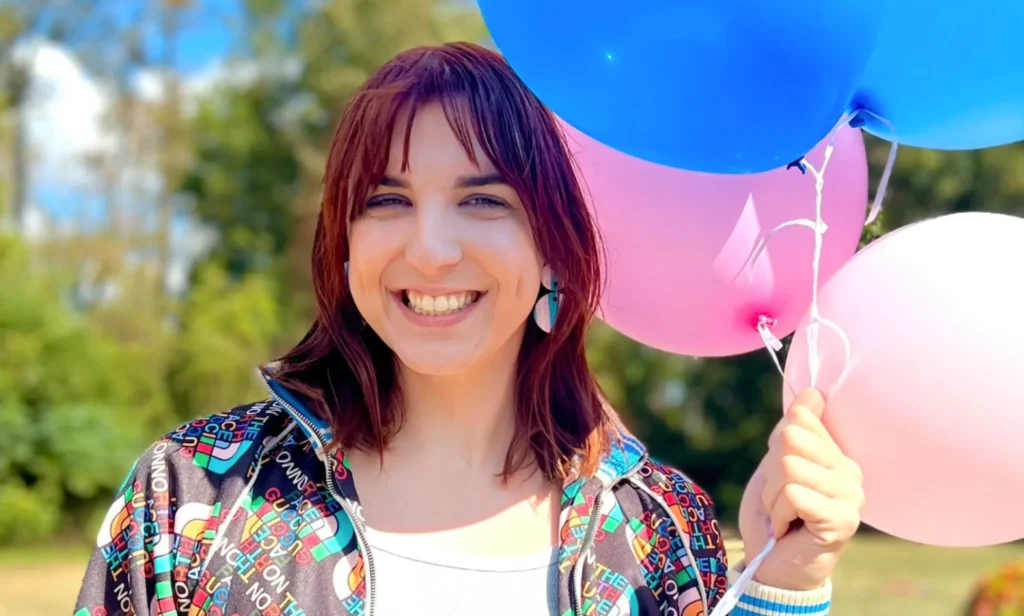 Kris Tyson, a YouTuber and MrBeast collaborator who is trans, smiles as she holds up pink and blue balloons next to her