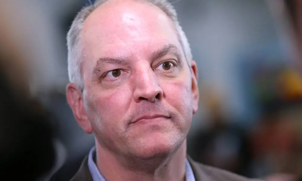 El gobernador de Luisiana, John Bel Edwards, mira ligeramente fuera de cámara mientras viste una camisa azul y una chaqueta gris.