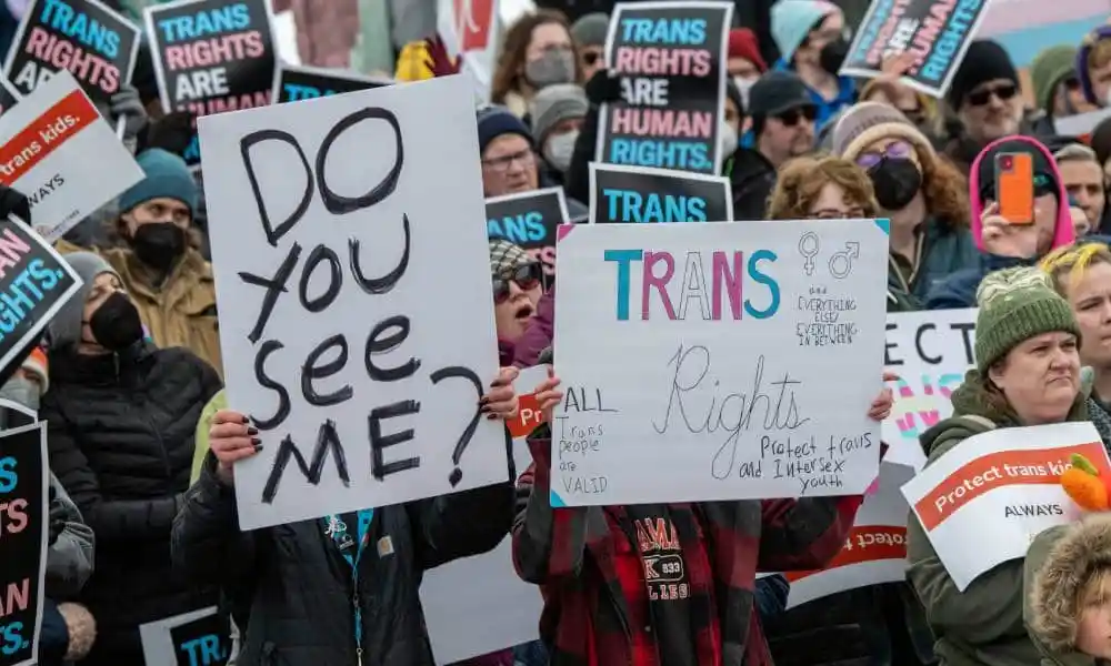 Several people protest in support of trans rights and condemning trans sports bans bills popping up across the US. One person carries a sign reading