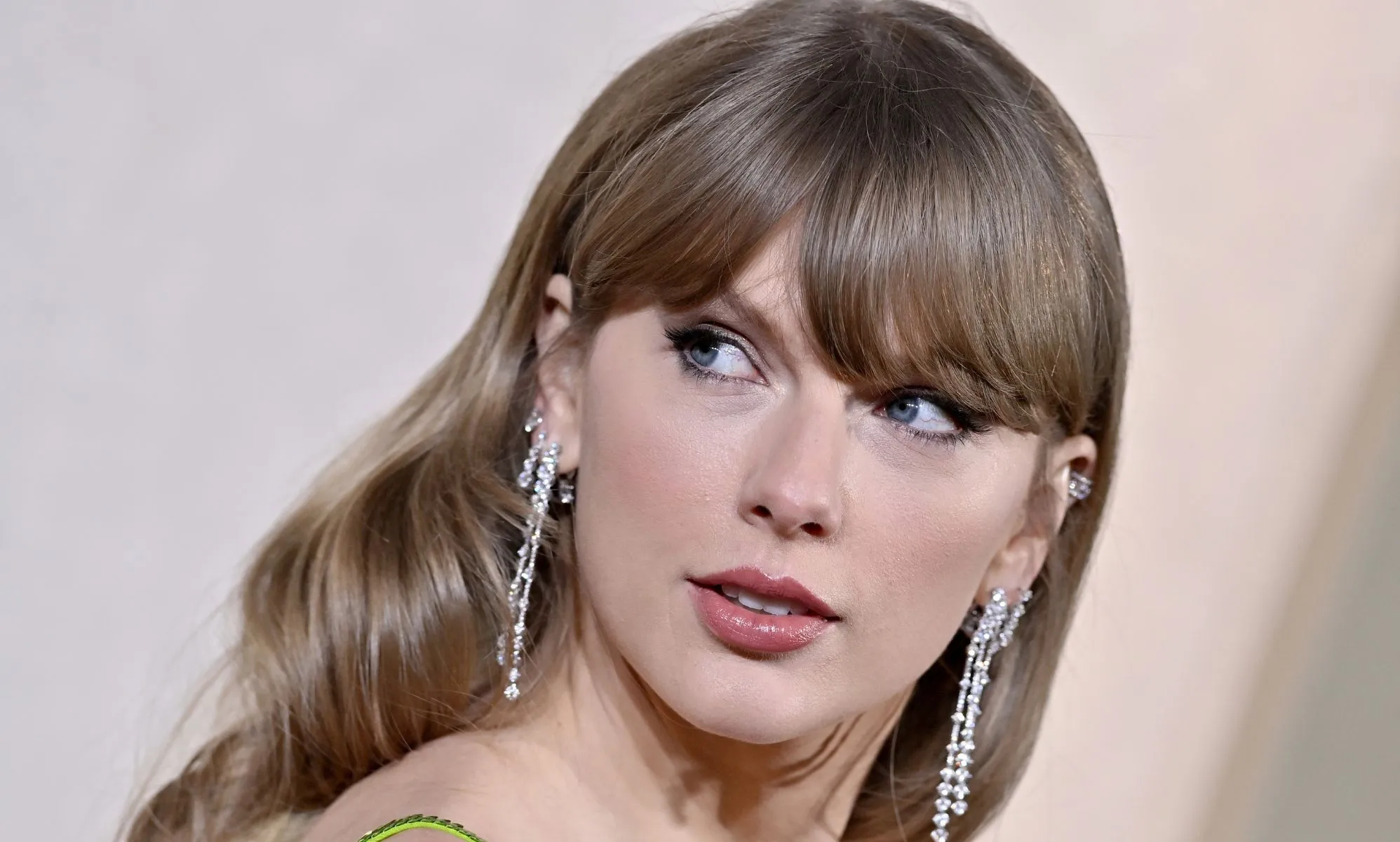 Taylor Swift looks over her shoulder as she wears a green dress and silver dangling earrings at an event