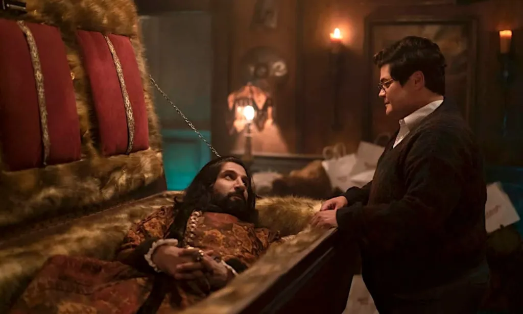 Una imagen fija de What We Do in the Shadows con el personaje vampiro Nandor en un ataúd con el familiar humano Guillermo hablando con él.