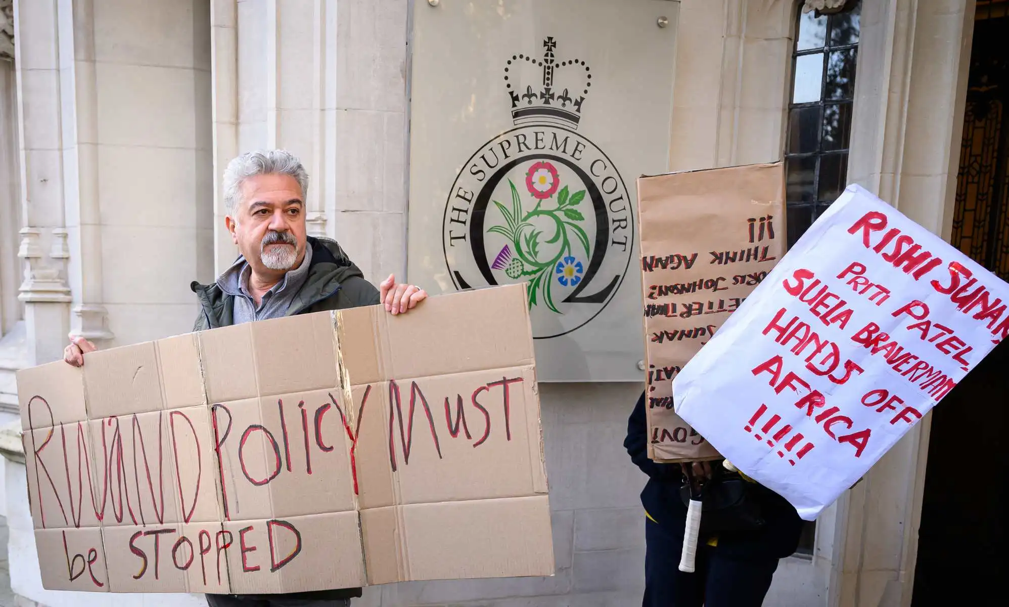 Activists hold posters with messages opposed to the Rwanda plan outside the Supreme Court.