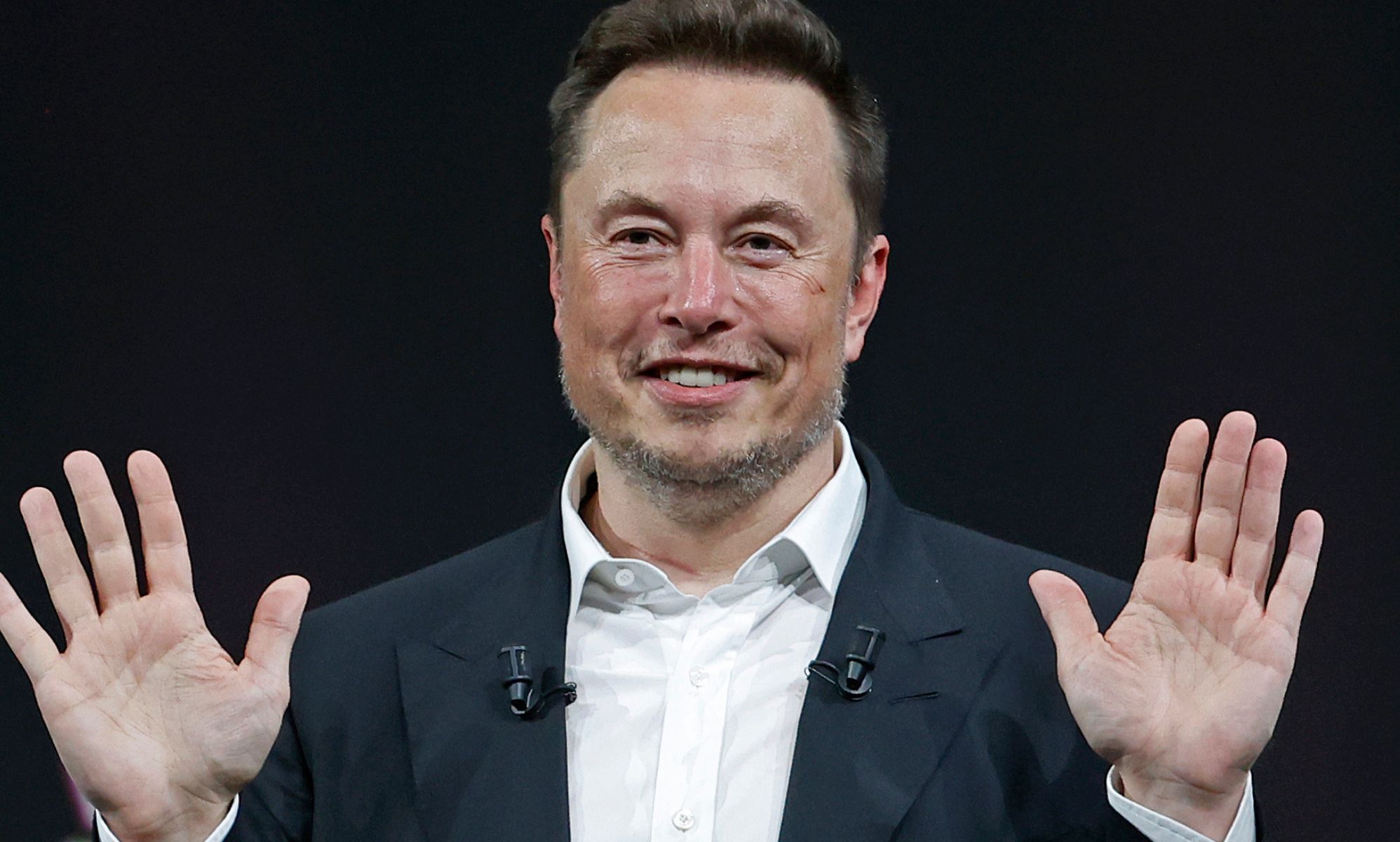 Elon Musk smiles with his hands raised.