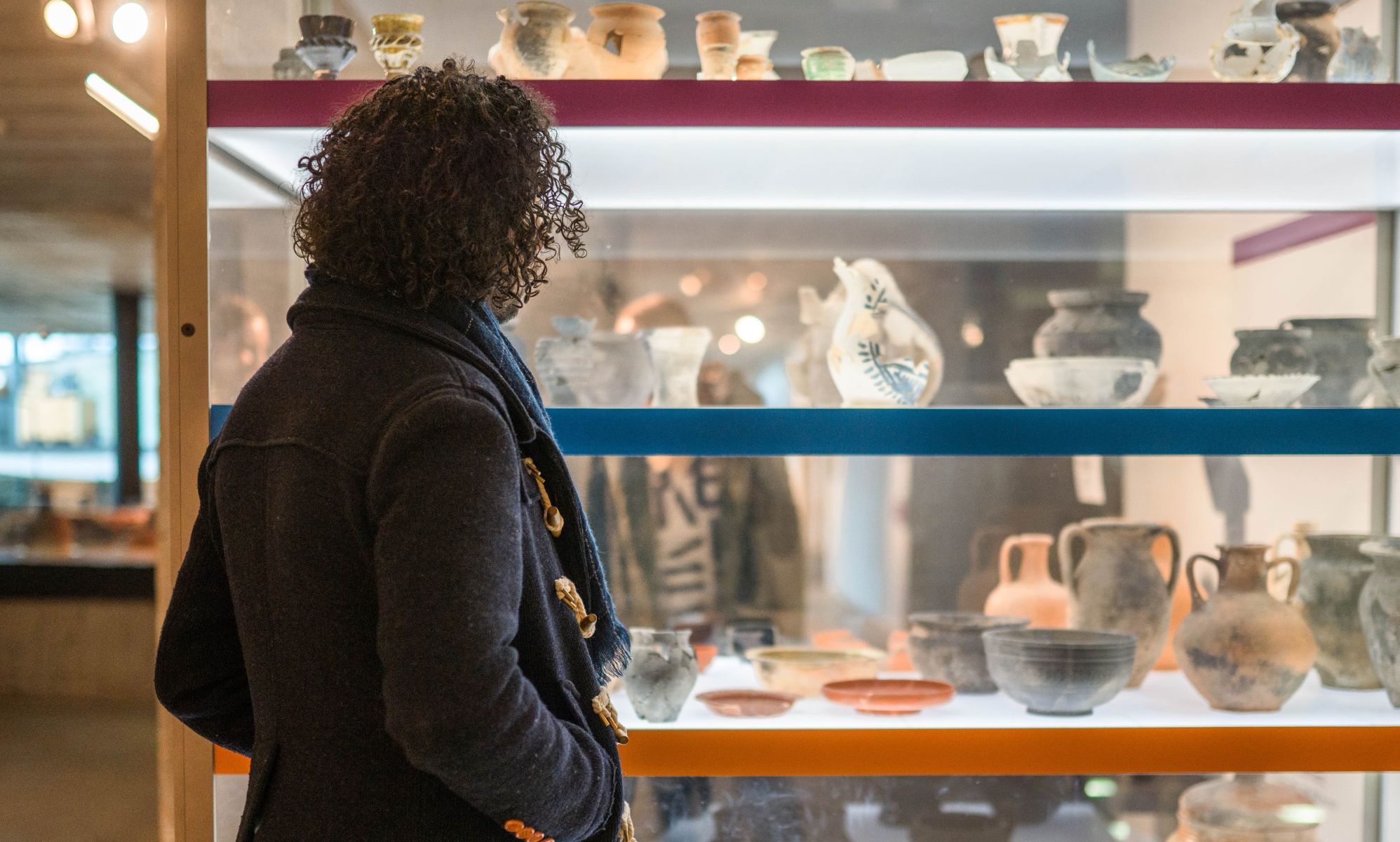 A woman stares and a museum exhibit with rows of ancient clay pots on display.