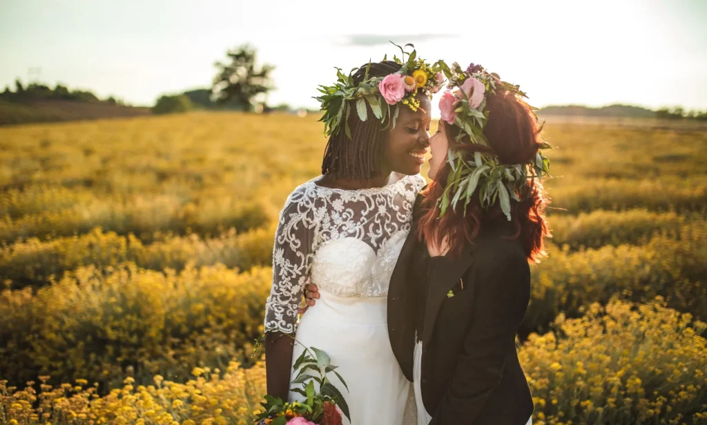 Stock image of a lesbian wedding, with one woman wearing a dress and carrying flowers, and another wearing a black suit jacket