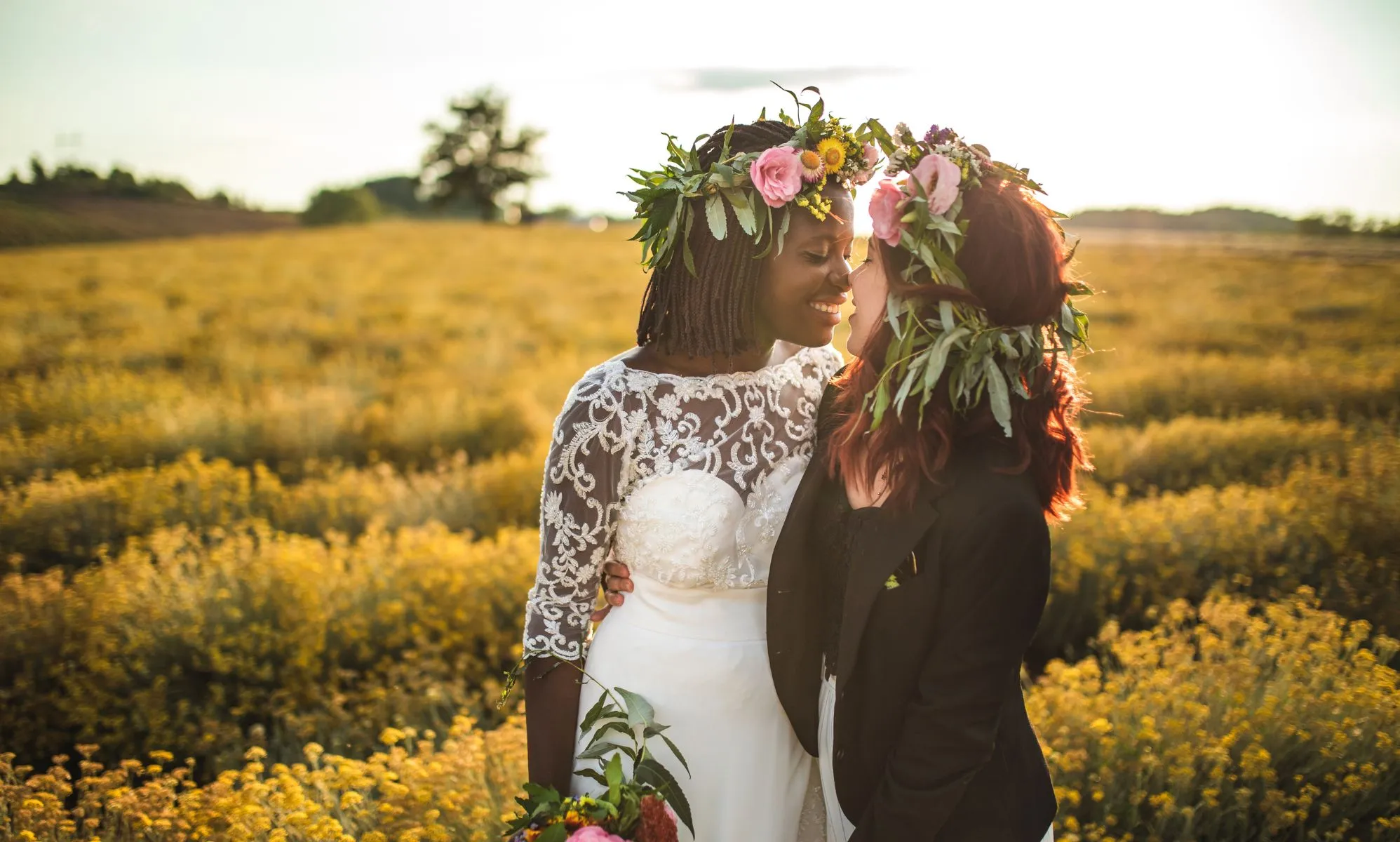 Stock image of a lesbian wedding, with one woman wearing a dress and carrying flowers, and another wearing a black suit jacket