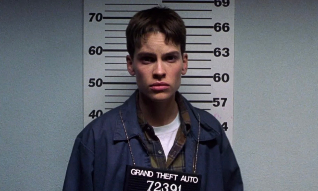 Hilary Swank como Brandon Teena recibiendo una fotografía policial en Boys Don't Cry.