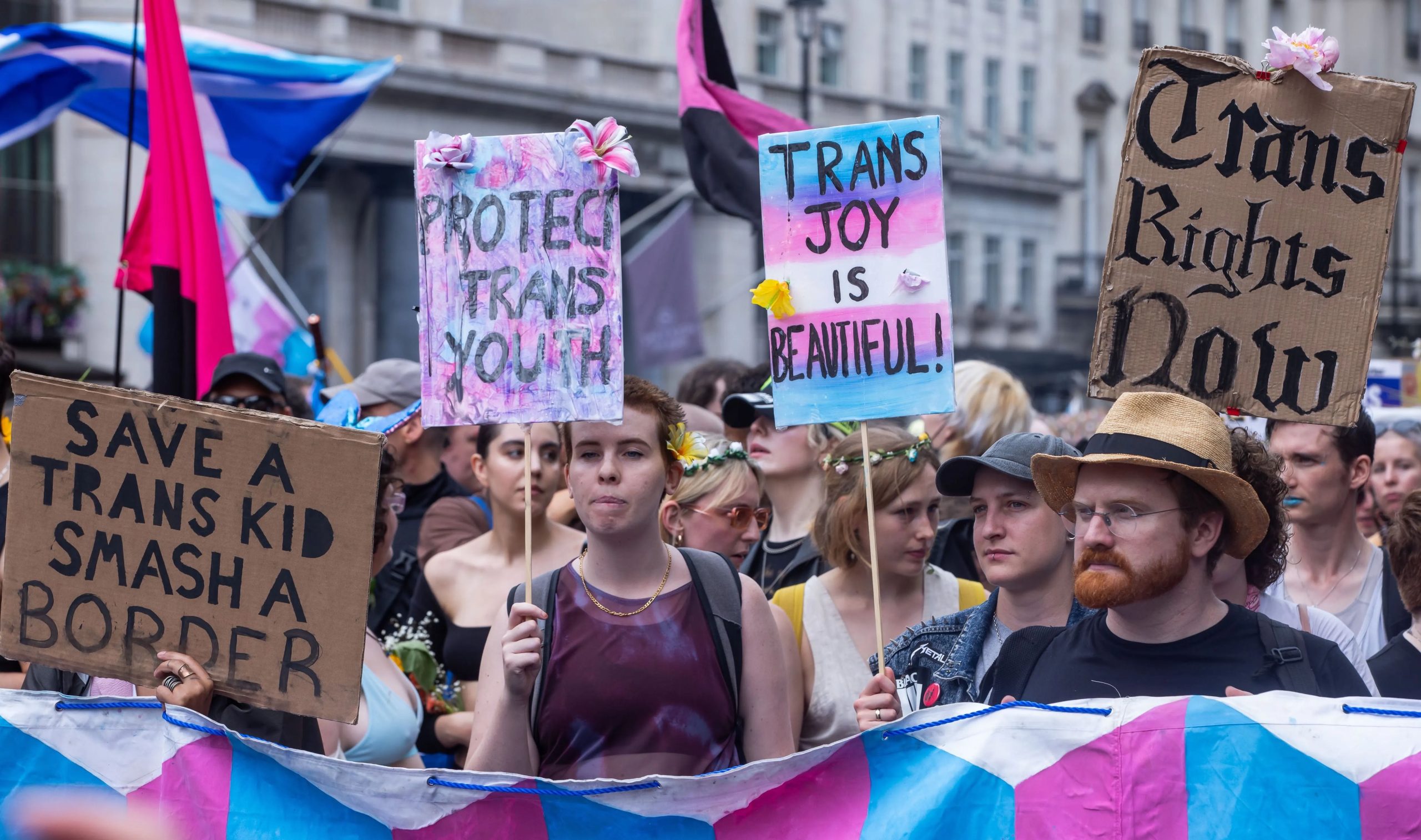 People walk down the street during a Pride march with signs reading