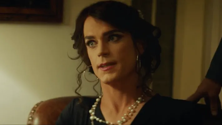 Matt Bomer interpreta al personaje trans Freda en Anything, Freda tiene el pelo oscuro recogido, aros y un collar de perlas.