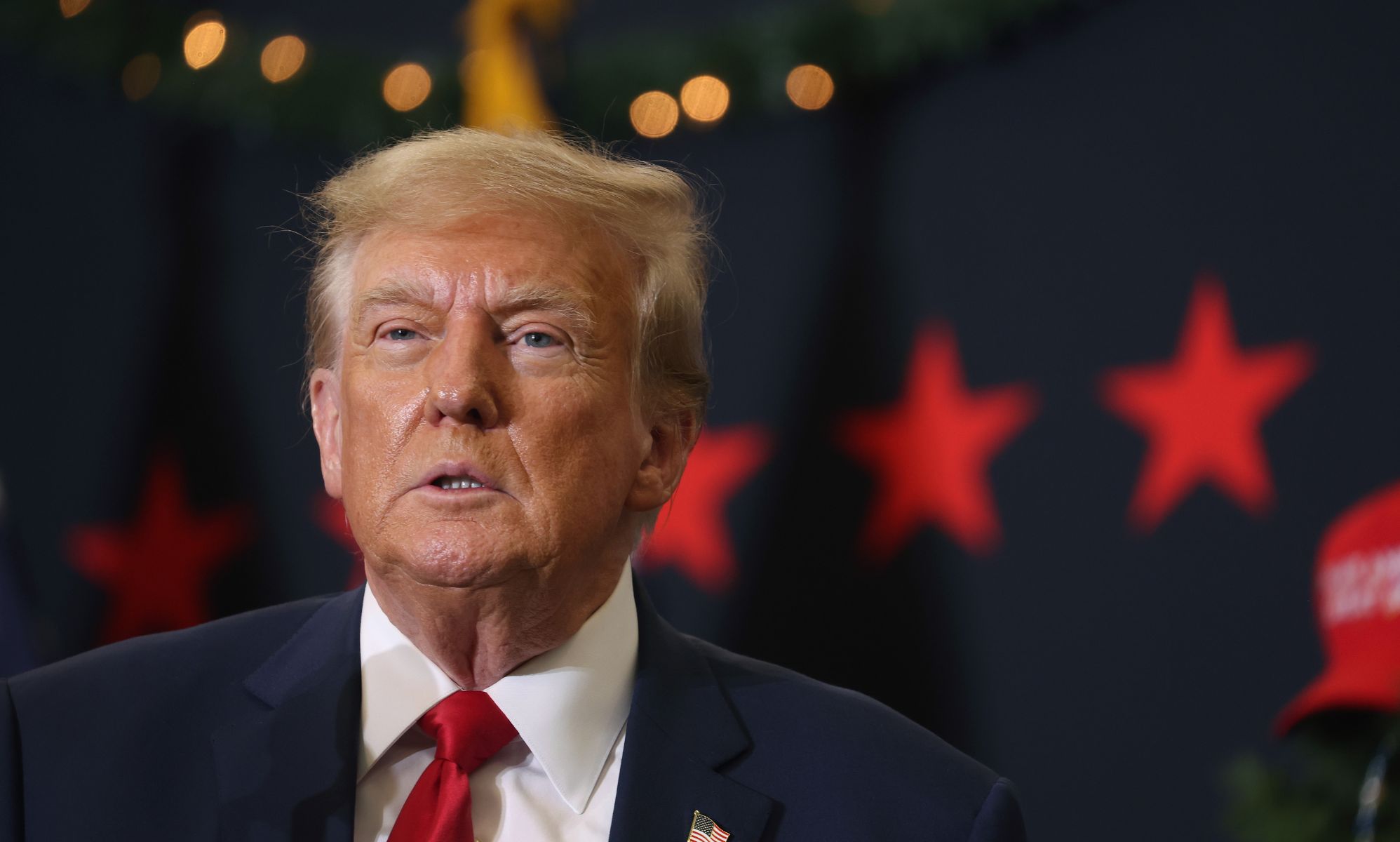 Former president Donald Trump wears a white shirt, red tie and dark blue jacket as he stares somewhere off camera