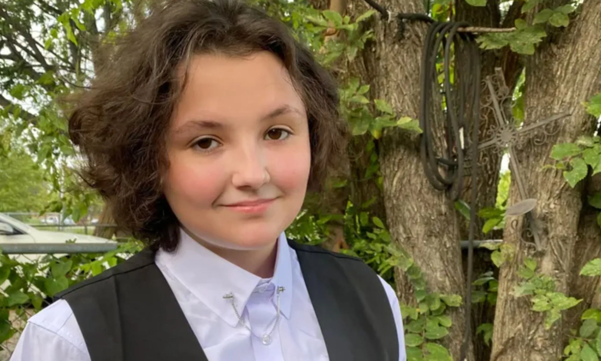 Oklahoma non-binary teen Nex Benedict, who died on 8 February 2024, wears a light coloured shirt and dark vest as they stand outside