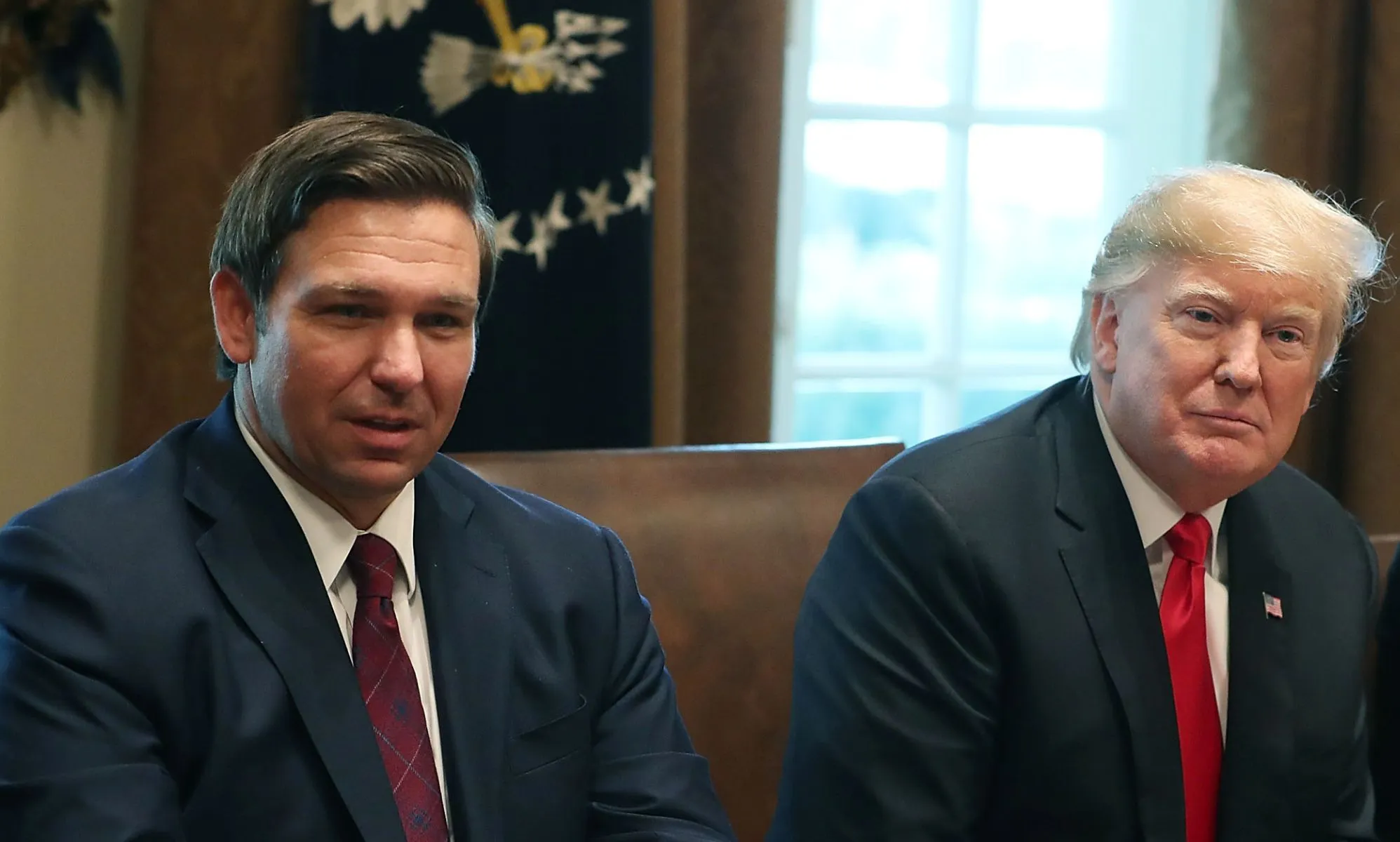 Republican politicians Ron DeSantis and Donald Trump sit side by side in the White House