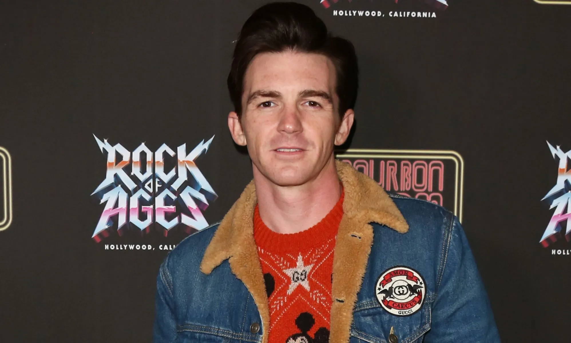Former Nickelodeon star Drake Bell wears a red shirt and jean jacket as he poses for the camera