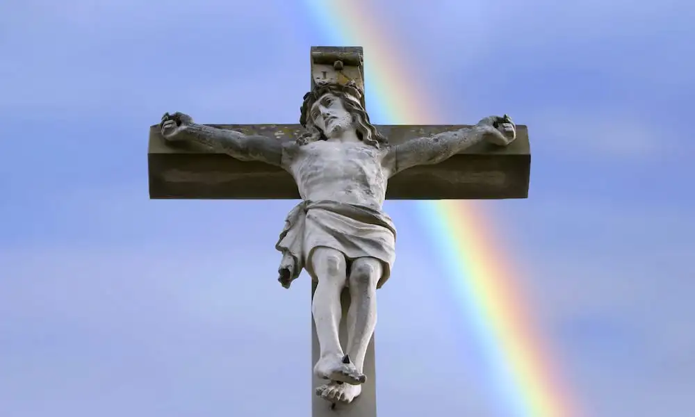 estatua de Jesús en un crucifijo frente a un arco iris