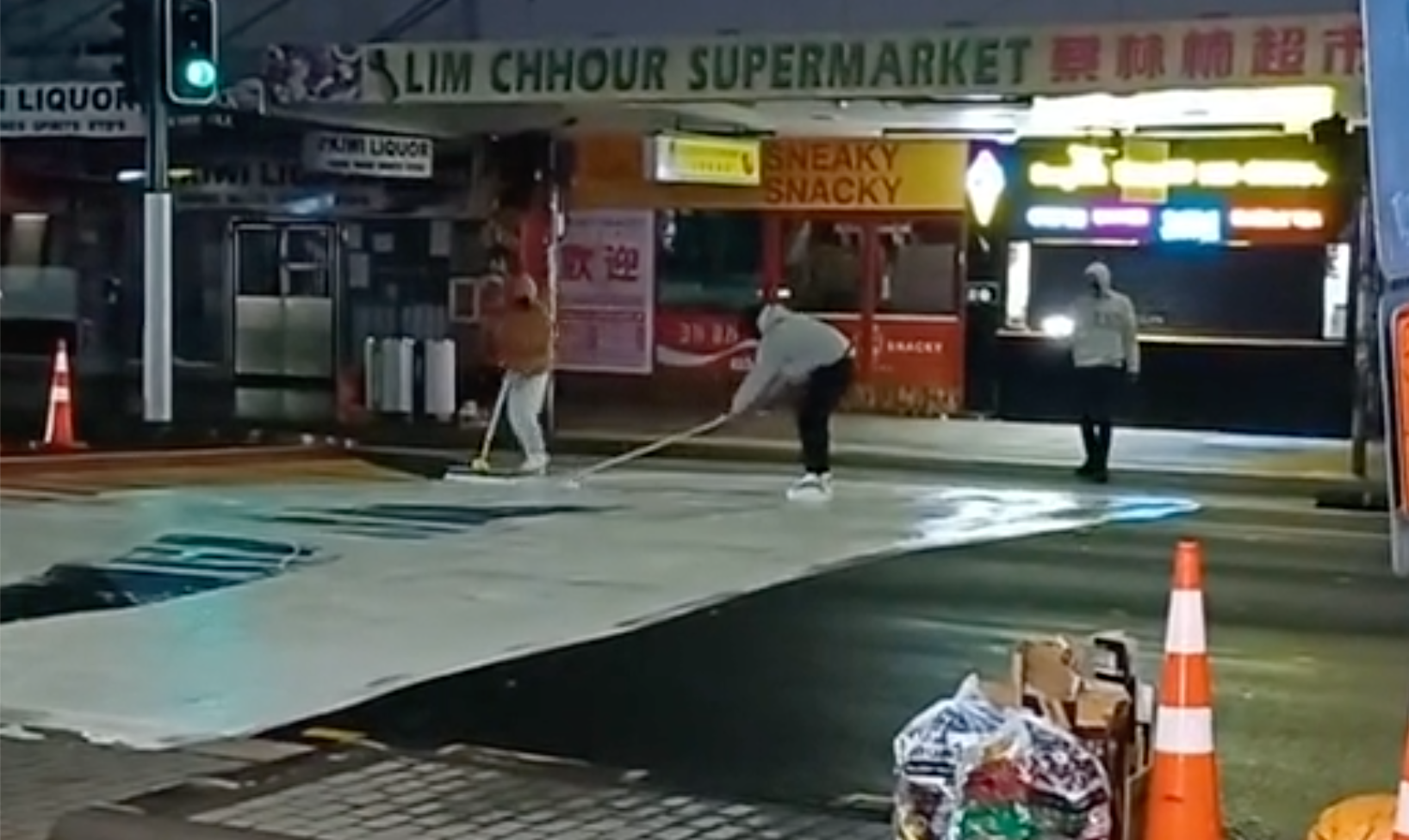 A video shows three people painting over a rainbow, Pride-themed crossing in Auckland