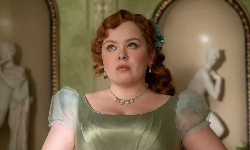 Nicola Coughlan wears a green dress and ginger hair in Bridgerton season three still. She is looking skyward and solemn.