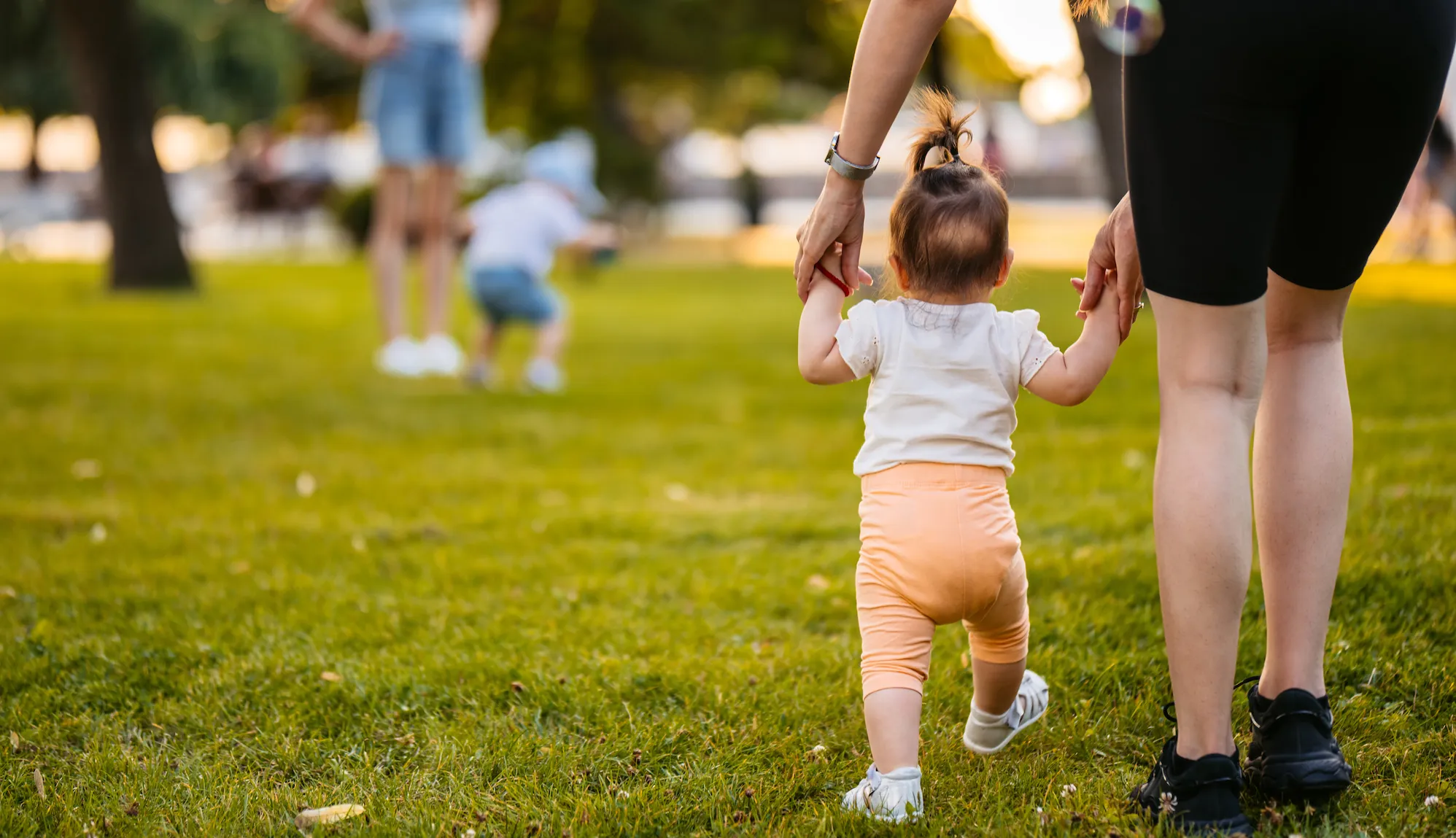 Young mother teaching her daughter how to walk in the park.