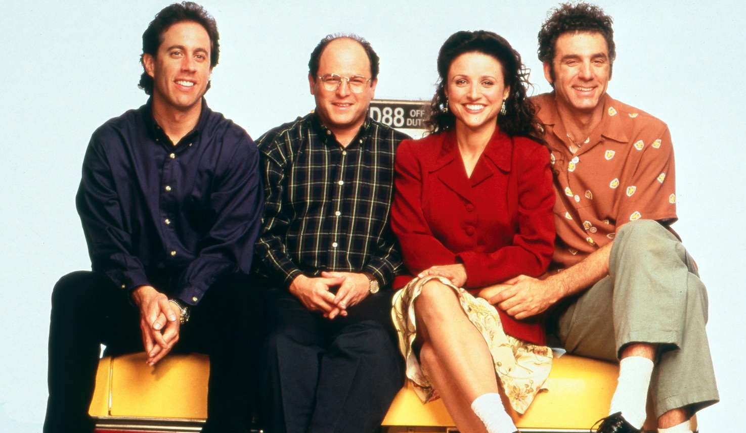 The cast of Seinfeld pictured in the 1990s sitting on a car.