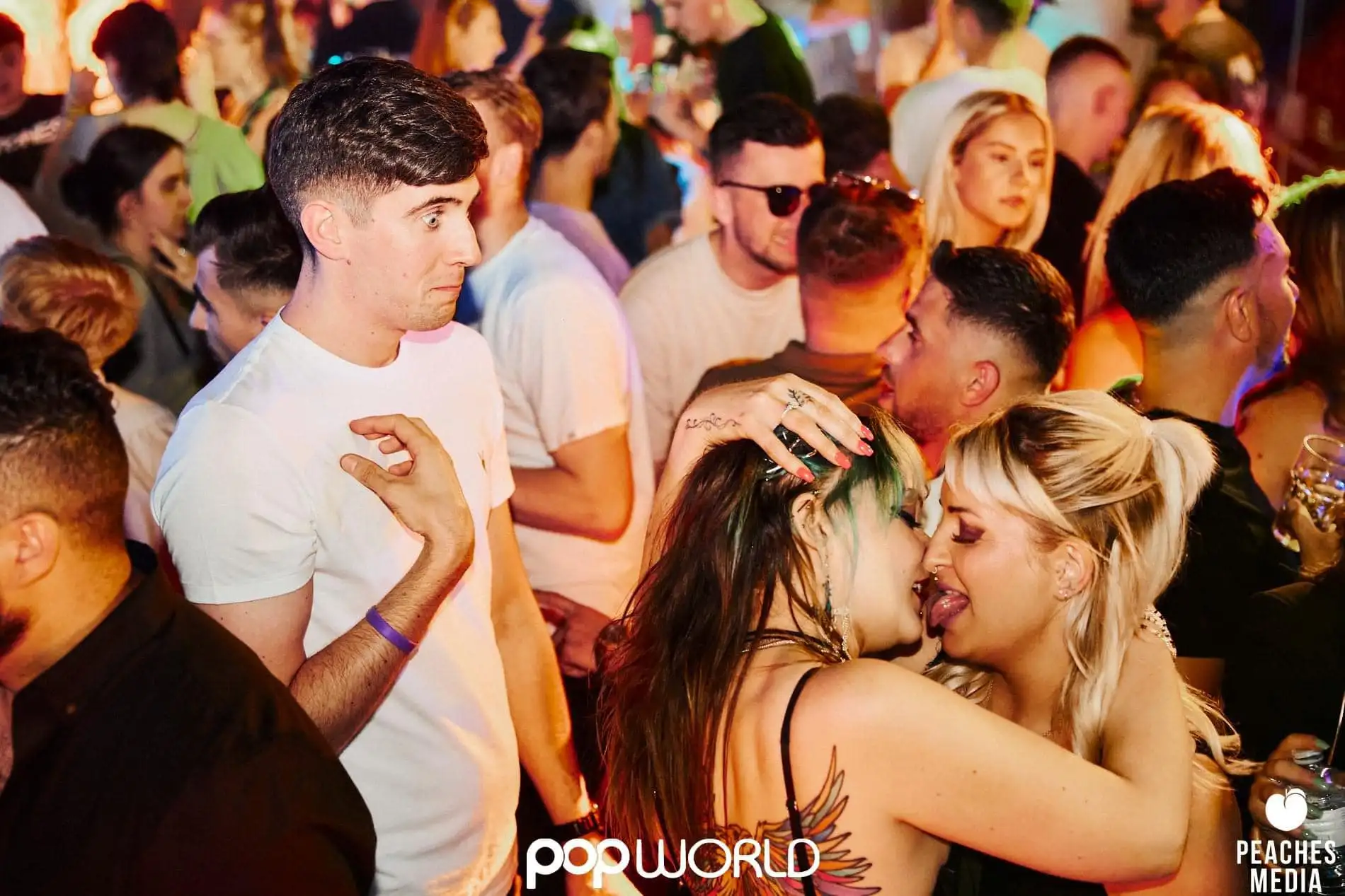 man looking on as two women kiss in popworld