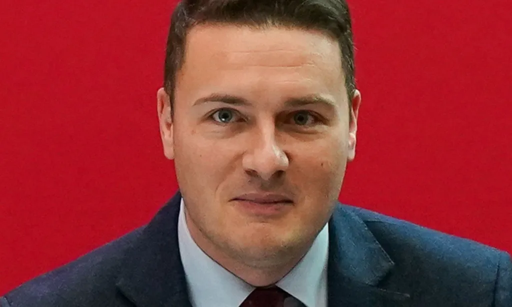 Wes Streeting en una conferencia laborista frente a un fondo rojo.