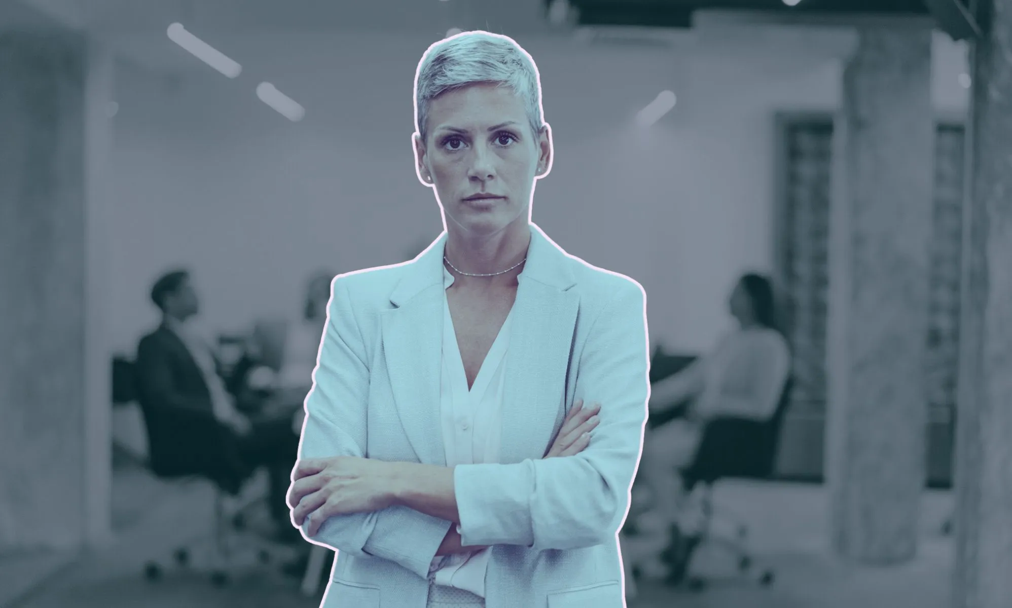 This is an image of an LGBTQ+ professional. She is a woman and she looks frustrated and her arms are folded. In the backgroud there are people in a meeting room.
