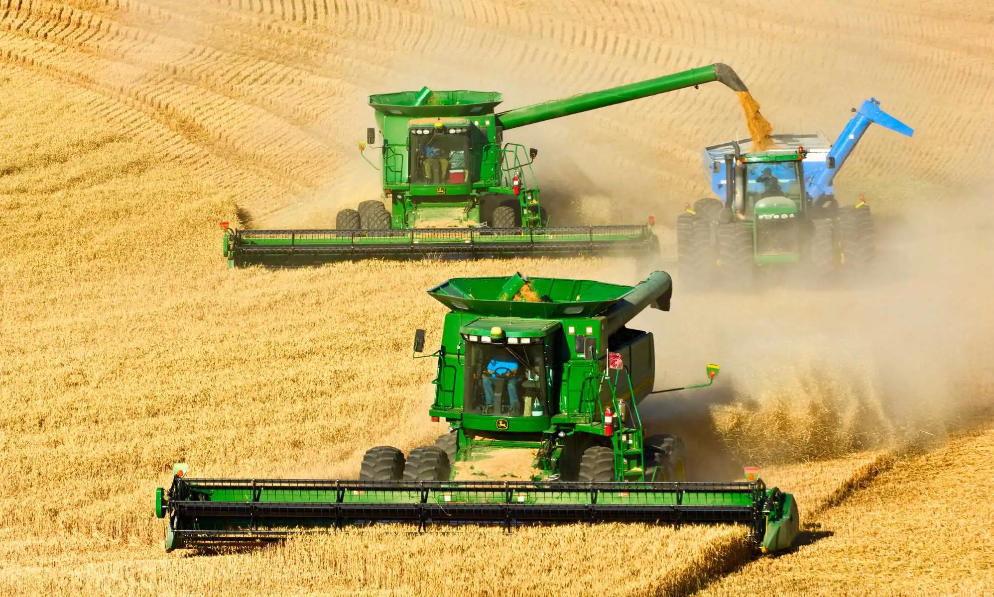 Agriculture - Two John Deere combines in tandem harvest wheat while one unloads into a grain cart. (Photo by: Rick Dalton /Design Pics Editorial/Universal Images Group via Getty Images)