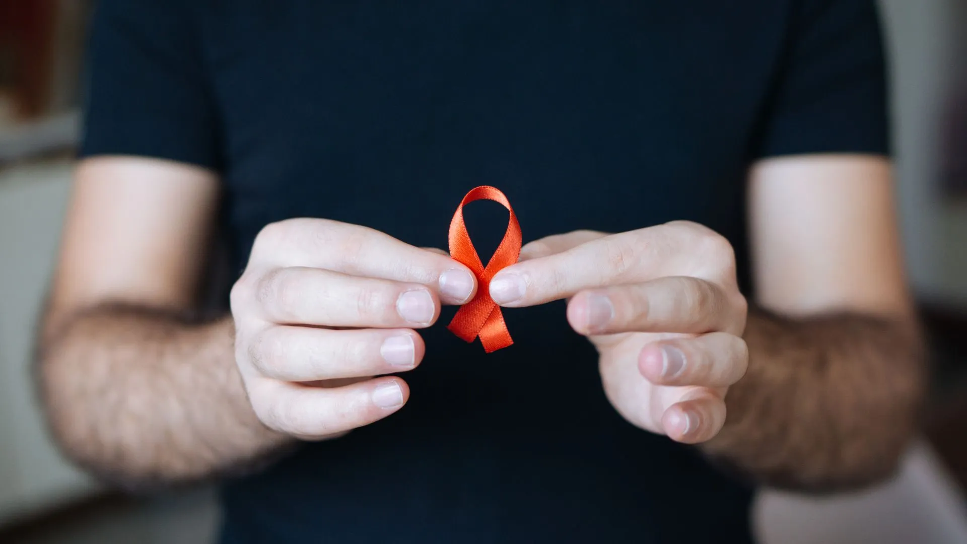 Person holding a red ribbon for HIV awareness