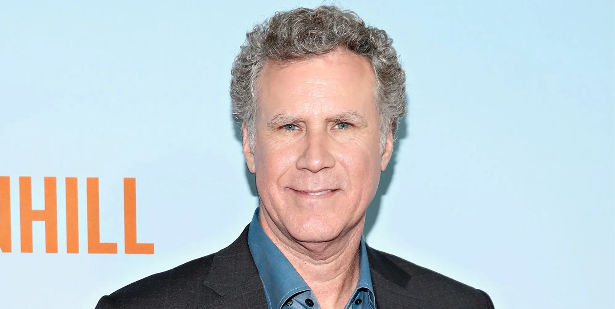 Will Ferrell smiles as he poses against a blue and orange red carpet background