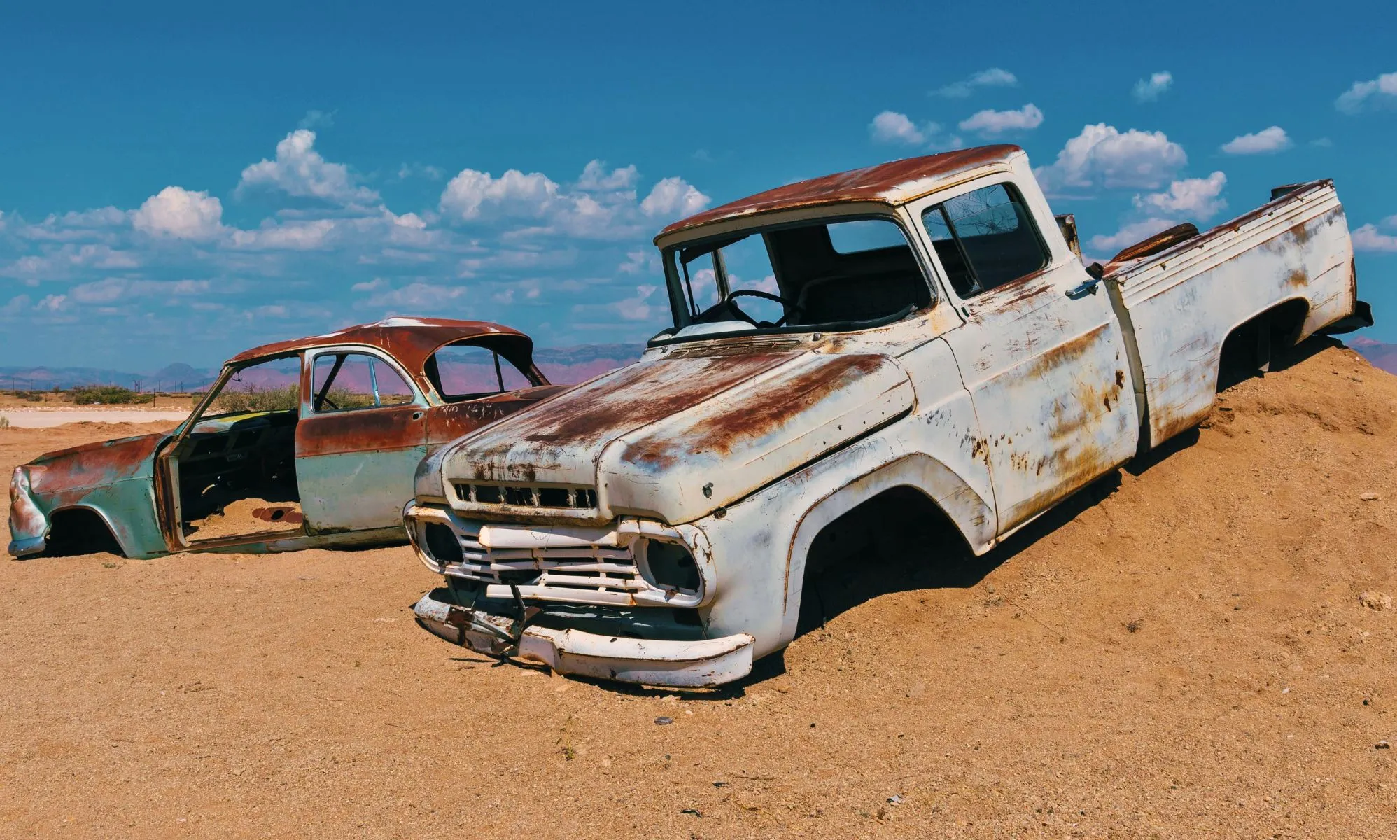 Two car husks sit on the mound of a desert hill.