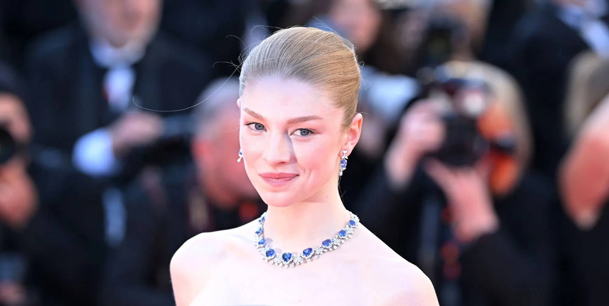 Hunter Schafer on a red carpet in a blue bejewelled necklace.