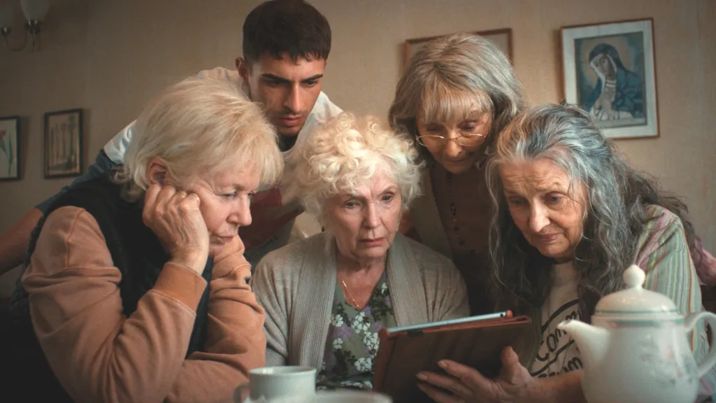 Cuatro madres de cuatro mujeres mayores mirando un iPad mientras un hombre más joven se les une