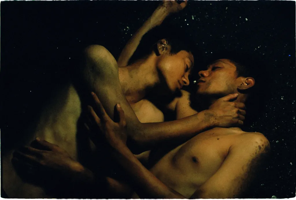 Vietnam y Vietnam aún, dos personas se abrazan en topless rodeados de oscuridad.