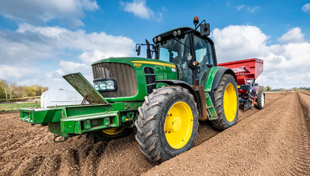 Siembra mecanizada de patatas de siembra utilizando una sembradora de cinta de tres hileras Dewulf detrás de un tractor John Deere.