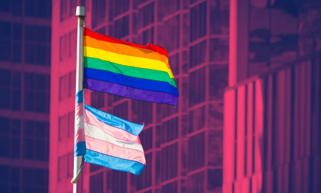 This is an image of the Pride flag flying above the Trans Pride flag outside an office building. The background has been altered to look fuschia.