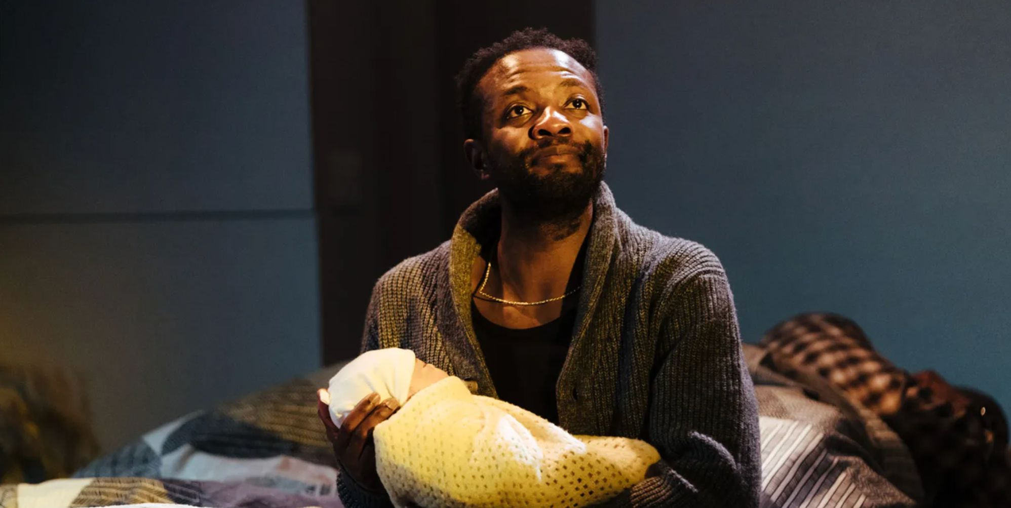 Omari Douglas holds a wrapped up baby in a photo from the set of Lavender, Hyacinth, Violet, Yew