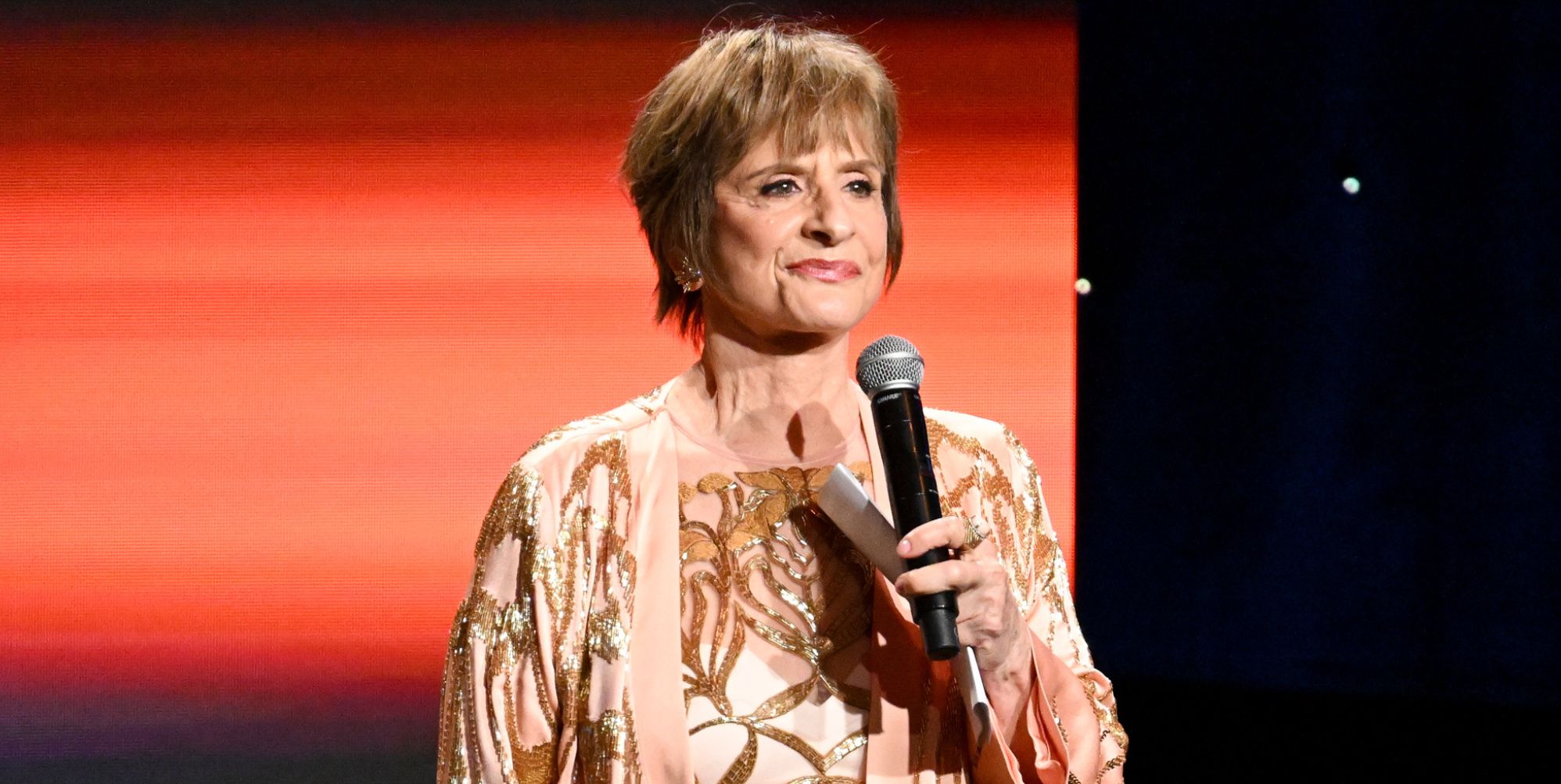Patti LuPone stands smiling with a microphone at the GLAAD Media Awards