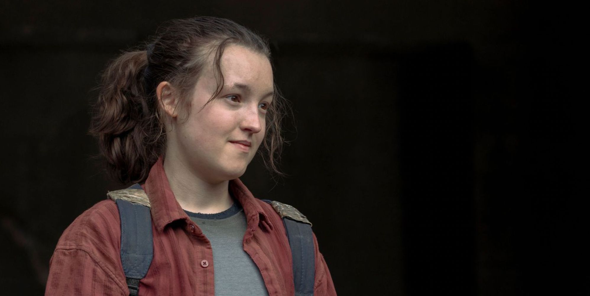 Bella Ramsey in a red shirt and wearing a backpack in role as Ellie in The Last of Us