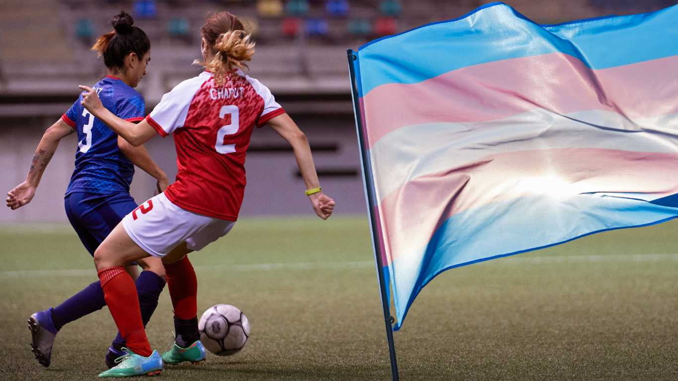 A still photograph of a female soccer defender in a blue uniform dribbling a soccer ball while an opposing attacker attempts to gain possession of the ball.