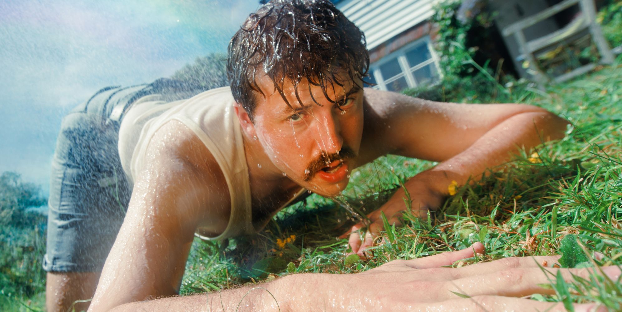 Kai Bosch lays on the grass wearing a white vest and blue jean shorts. He is dripping wet.