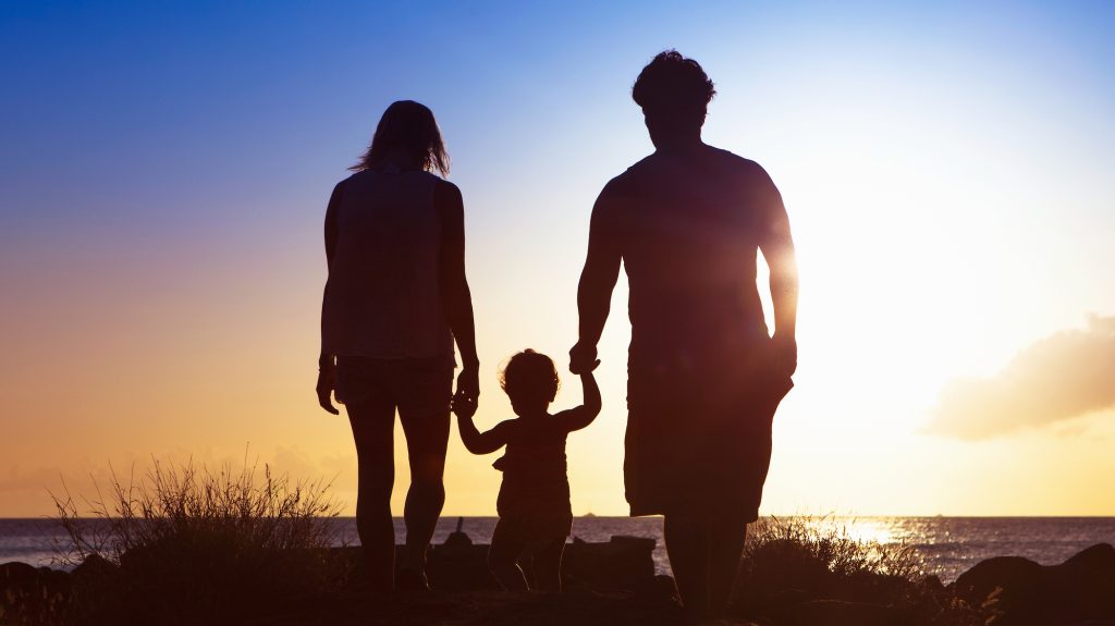 A family walks into the sunset on the beach with their two year old daughter.