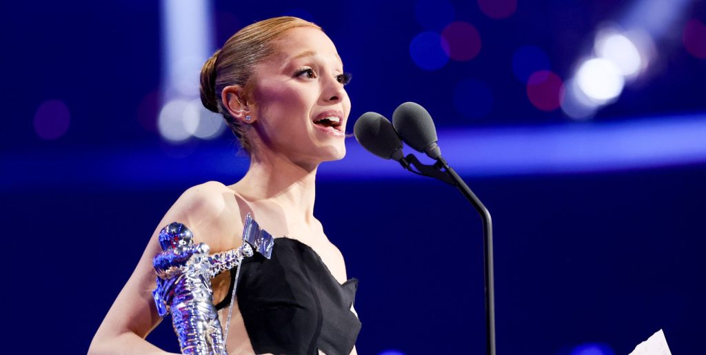 Ariana Grande holding a moon person statue and speaking into a microphone as she accepts a video music award.