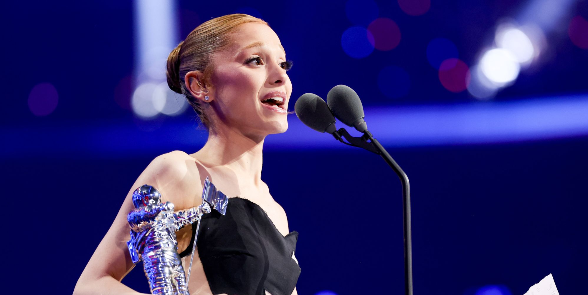 Ariana Grande holding a moon person statue and speaking into a microphone as she accepts a video music award.