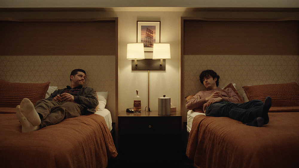 Dylan O'Brien y James Sweeney estrella en Twinless. Los dos hombres están acostados en camas de hotel separados.